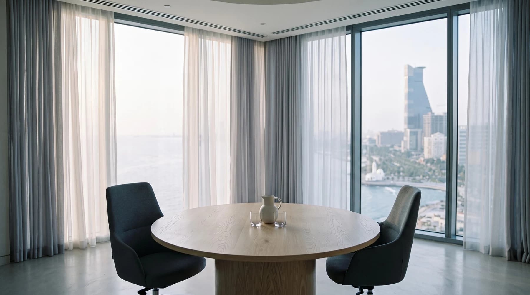 A calm meeting room with a round oak table and two chairs, overlooking the sea.