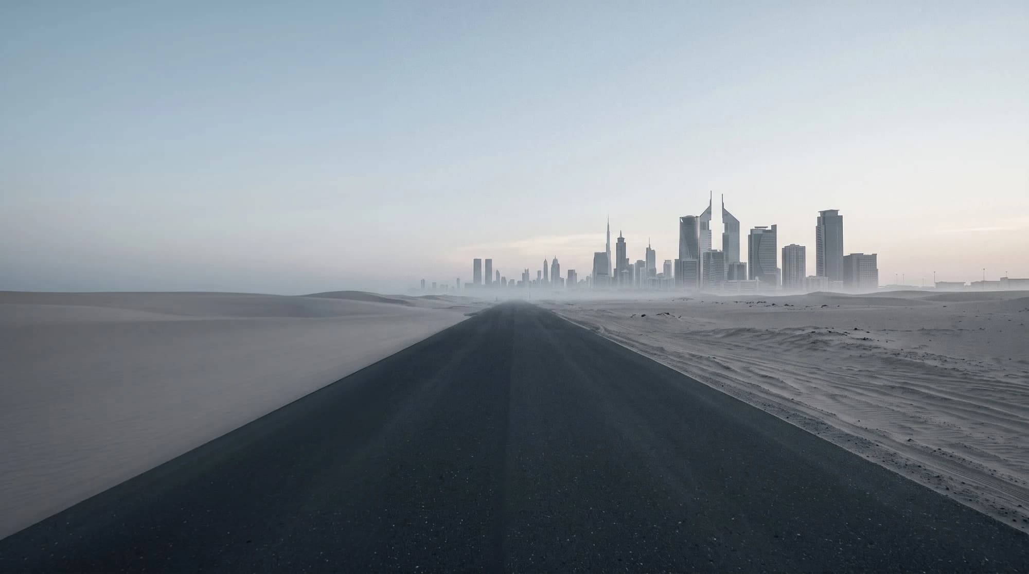 A straight desert highway at dawn, leading toward a distant city skyline.